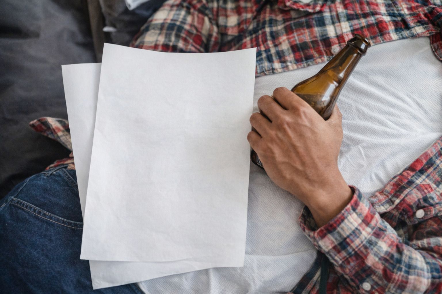 En mand i ternet skjorte holder en ølflaske og hvide papirer.
